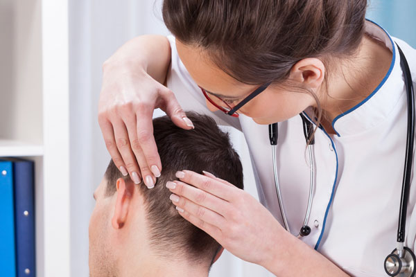 Ärztin untersucht Kopfhaut von Patient